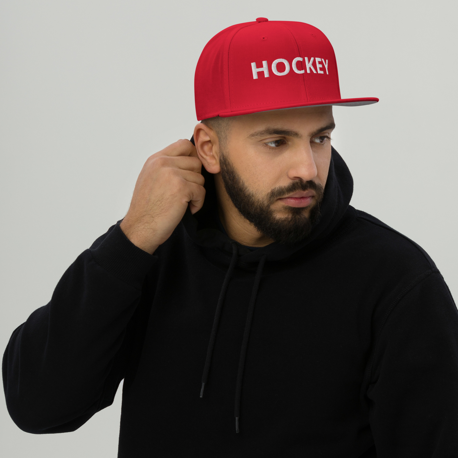 Mann trägt rote HOCKEY Snapback-Cap mit weißem Schriftzug und schwarzem Hoodie